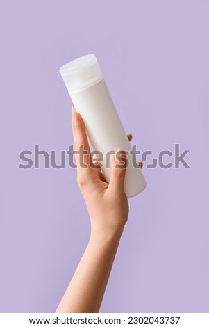 Hand holding cosmetic product on lilac background Royalty-Free Stock Photo #2302043737