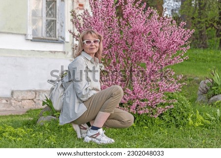 Mature adult attractive woman on the background of blooming bush of steppe almond with delicate pink flowers.