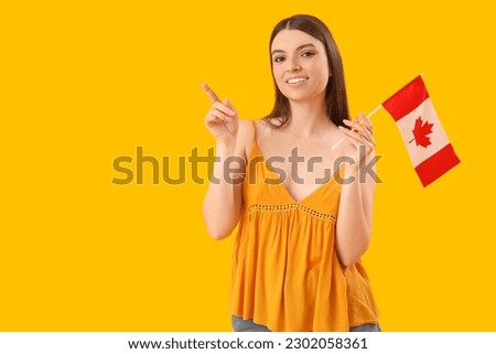 Young woman with flag of Canada pointing at something on yellow background
