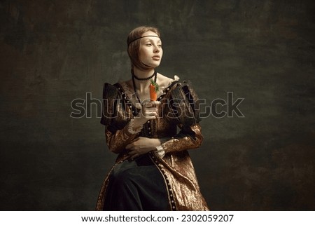 Portrait of young girl, princess, royal person in vintage dress posing with carrot against dark green background. Healthy diet, vitamins, Concept of history, renaissance art remake, comparison of eras