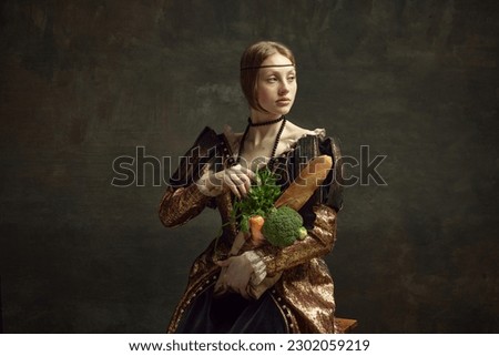 Portrait of young beautiful girl, princess in vintage, elegant costume with baguette and vegetables on dark green background. Concept of history, renaissance art, comparison of eras. Grocery shopping
