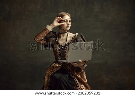 Portrait of young girl, royal person, princess in vintage dress and modern glasses working on laptop against dark green background. Concept of history, renaissance art remake, comparison of eras Royalty-Free Stock Photo #2302059231