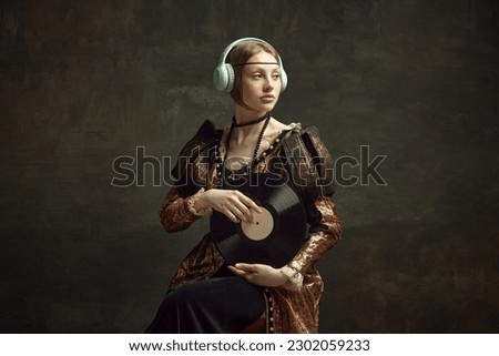 Portrait of pretty young girl, royal person in elegant vintage dress listening to music in headphones, holding vinyl on dark green background. Concept of history, renaissance art, comparison of eras Royalty-Free Stock Photo #2302059233