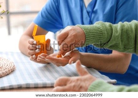 Young caregiver and senior woman taking pills in kitchen, closeup Royalty-Free Stock Photo #2302064999
