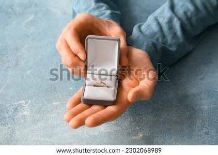 Man holding box with engagement ring on blue background Royalty-Free Stock Photo #2302068989