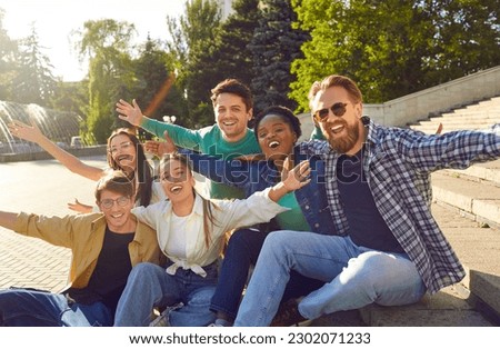 Bunch of happy multiracial friends having fun outdoors. Diverse group of cheerful joyful young people sitting on stone steps on beautiful small city square, looking at camera and smiling all together Royalty-Free Stock Photo #2302071233