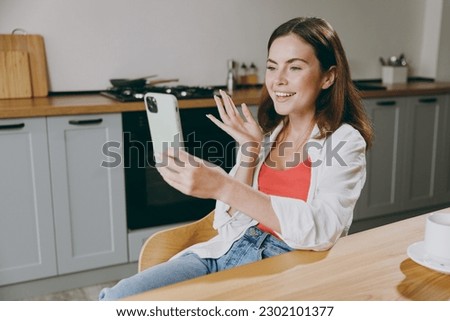 Young housewife woman wear casual clothes doing selfie shot on mobile cell phone eat breakfast muesli cereals with milk fruit in bowl cooking food in light kitchen at home alone. Healthy diet concept