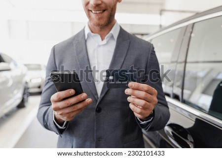 Cropped up photo man male client buyer in classic suit choose auto want buy new car automobile hold credit bank card talk mobile phone in showroom salon dealership store motor show indoor Sale concept
