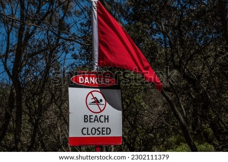 A sign shows beach closed and a red flag in front an agitated ocean