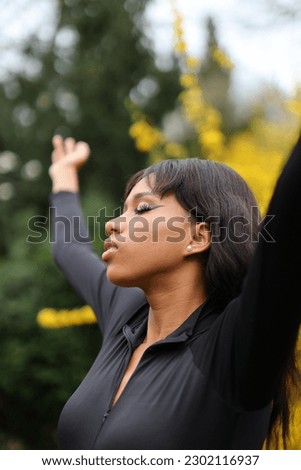 A woman with closed eyes raised her hands up on the background of nature relaxation and meditation.