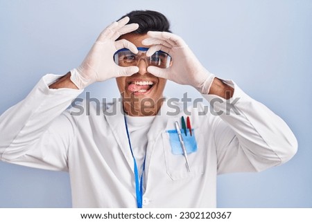 Hispanic man working as scientist doing ok gesture like binoculars sticking tongue out, eyes looking through fingers. crazy expression. 