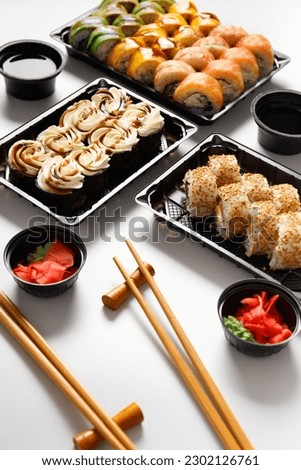 Set of sushi rolls in plastic takeaway packages with soy sauce, ginger, wasabi and chinese chopsticks on a white background. Delivery of sushi in a plastic container