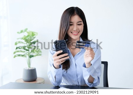 Smiling cute asian woman using credit card and smartphone, paying bills online, holding mobile phone, looking at camera.