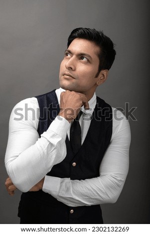 Studio shot of cheerful, young, handsome  Indian business man in formal wear against grey background. Male model. Fashion Portrait.
