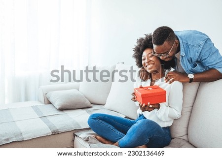 African descent brazilian couple exchanging gifts at home. Surprised woman receiving Birthday present from her boyfriend. Young happy woman being surprised by her boyfriend with a birthday preset. 