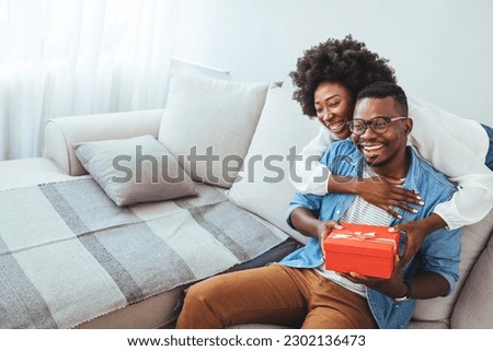 Happy young diverse couple celebrating Valentine's day together at home, with boyfriend buying a Valentine's present to his girlfriend, making her feel loved and special