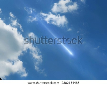 Meteor glows in the blue sky at daytime. Fireball between the clouds in the light of the sun.