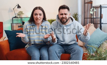 What. Why. Young family married couple man woman raising hands in indignant expression, asking reason of failure, demonstrating disbelief irritation by troubles at home. Husband wife together on sofa Royalty-Free Stock Photo #2302160481