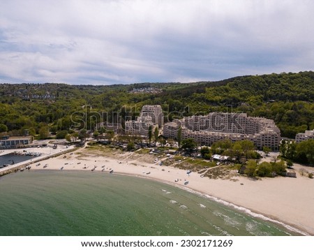 drone's eye view of the beach, sea, boat dock, modern hotel, and forest in the distance. Perfect for vacation, travel, and leisure lovers seeking a serene and picturesque escape