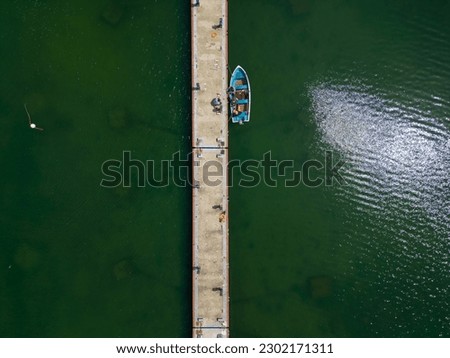 aerial view of a serene dock in the sea, with several fishing boats tied up and bobbing in the calm waters. It's a peaceful scene that captures the essence of coastal living.