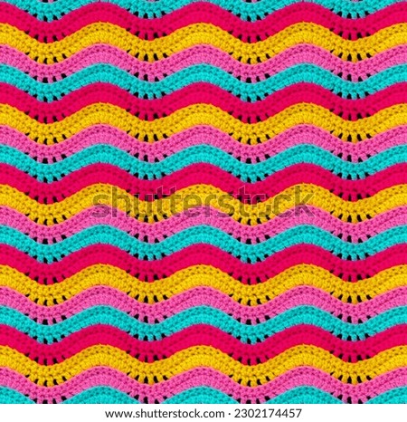Seamless knitted pattern in the form of openwork waves is crocheted with threads of bright colors. Acrylic baby yarn. Volumetric style.