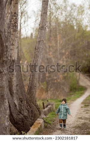 
Toddler walks in the park with huge trees in early spring