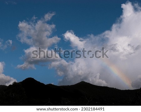 Silhouette of an andean mountain with a segment of a rainbow and clouds