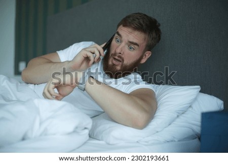 Young sleepy awaken man is just wake up with phone call, looking at his watches checking time and hurry up and yawn. Guy overslept job  Royalty-Free Stock Photo #2302193661