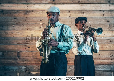 Two african american jazz musicians playing trumpet and saxophone. Standing in front of old wooden wall. Royalty-Free Stock Photo #230219902