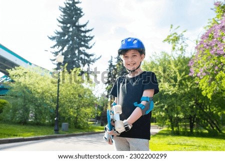 portrait of a boy in a purple safety helmet, holds a blue plastic city cruiser, skateboard, in a sunny park in summer