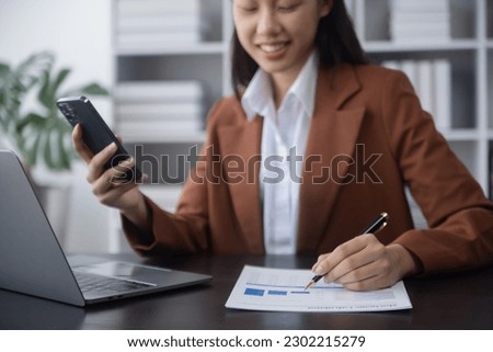 young Asian businesswoman holding a smartphone and working  with computer at table office, Businesswoman secretary employee working online at desk in company office.