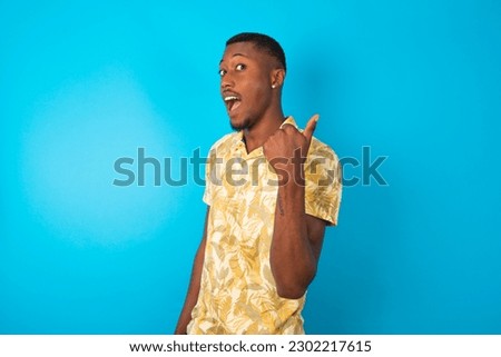Impressed young man wearing Hawaiian yellow T-shirt over blue background point back empty space