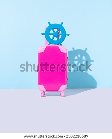 Pink suitcase and rudder ship with shadows. Minimal summertime composition. Concept of travel and vocations. Blue grey background. front view.