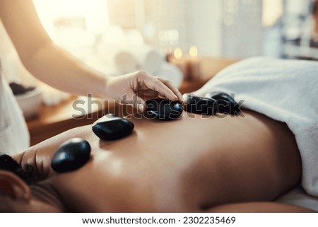 Woman, hands and rocks for back massage at spa in beauty relaxation or skincare on bed. Hand of masseuse applying hot rock or stones on female for physical therapy, zen or skin treatment at resort Royalty-Free Stock Photo #2302235469