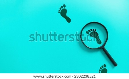 Magnifying glass magnifying black bare footprints on blue background. Investigation and detective concept.