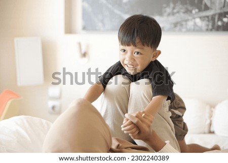 young asian mother and son playing on bed cheerfully in hotel room on vacation