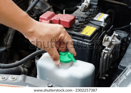 Closeup hand hold bottle tank of car engine coolant. Concept, automobile maintenance. Check and repair before driving for safety. Basic diagnose vehicle problems.           Royalty-Free Stock Photo #2302257387