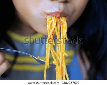Close up daughter eat spaghetti with garp, spaghetti lifted and long.
