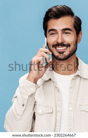 Portrait of a brunette man close-up talking on the phone smile with teeth joy looks at the camera, on a blue background in a white T-shirt and jeans, copy space