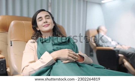 Young Hispanic latino woman passenger sleeping on seat with blanket while traveling by airplane. Woman travel on long flight Royalty-Free Stock Photo #2302264819
