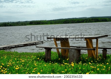 A bench by the water. A wooden bench with a table on the shore of the lake, the sea. for a family holiday on the beach. Close-up.natural background.Creative image. postcard.