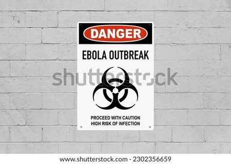 Black, red and white danger sign attached on a brick wall painted in grey. The sign stating “Danger - Ebola outbreak - Proceed with caution, high risk of infection”.