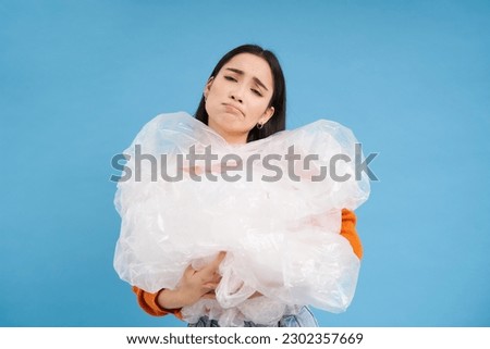 Asian sad woman holding plastic garbage and frowning from disappointment, fighting polution, eco-activist sorting waste, blue background.