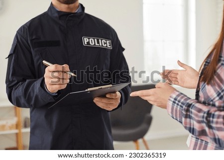 Policeman interrogating woman or witness regarding police investigation. Male police officer in uniform writing down testimonies to investigate burglary. Police investigation concept Royalty-Free Stock Photo #2302365319