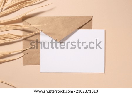 Closeup of blank card mock-up and craft envelope and dry palm leaf. Flat lay, top view, tropical vacation concept.