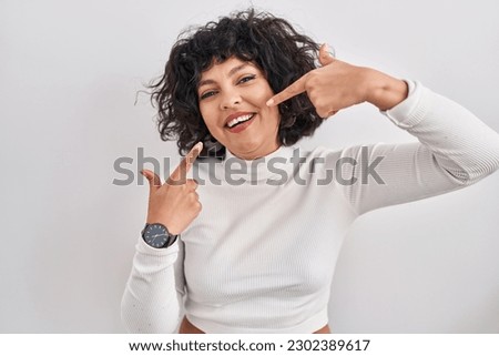 Hispanic woman with curly hair standing over isolated background smiling cheerful showing and pointing with fingers teeth and mouth. dental health concept. 