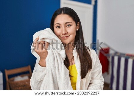 Young hispanic woman touching face with soft towel at laundry room