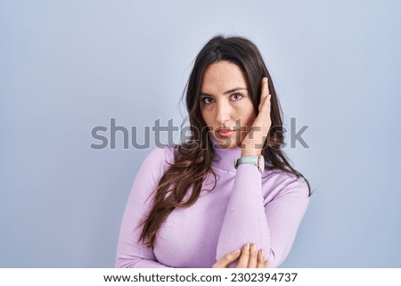 Young brunette woman standing over blue background thinking looking tired and bored with depression problems with crossed arms. 