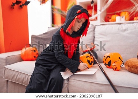 Adorable caucasian boy wearing halloween costume drawing on paper at home