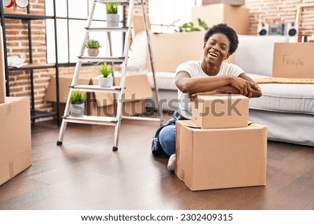 African american woman sitting on the floor at new home smiling and laughing hard out loud because funny crazy joke. 